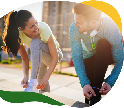 A woman and a man looking at each other while kneeling on the side of the road and tying their jogging shoes