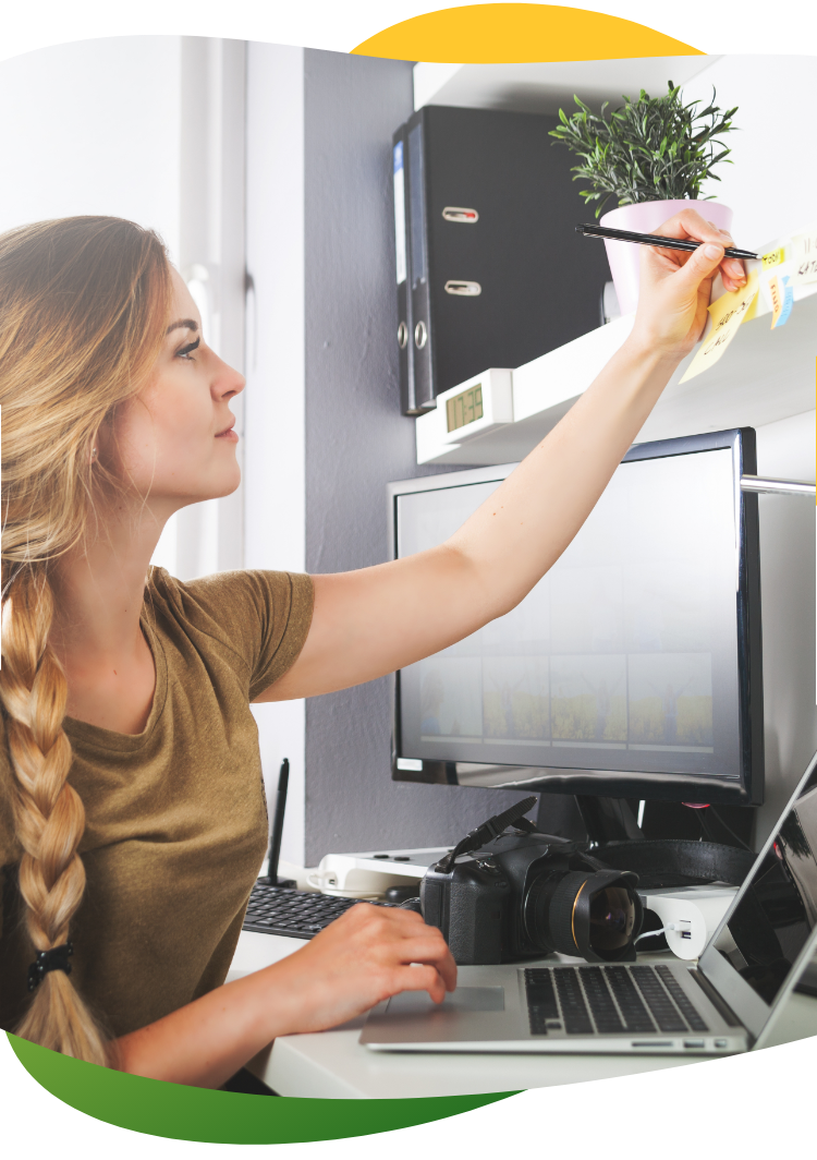 A young woman with blonde braided pigtail sits at her desk making notes on her post it